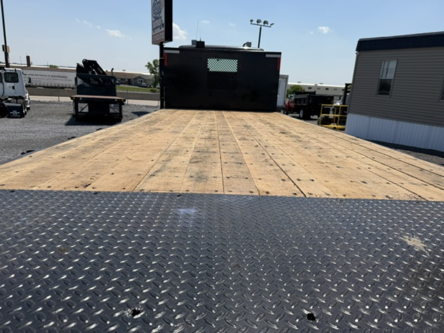 Flatbed truck bed of a 2016 Freightliner M2-112 showing wooden deck and metal diamond plate ramp.