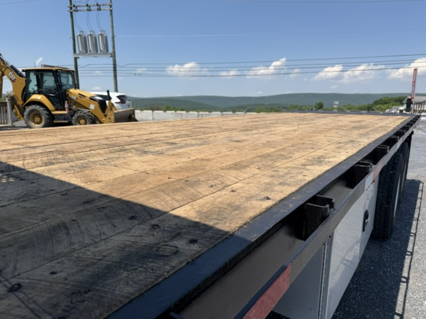 Flatbed truck bed of a 2016 Freightliner M2-112 with wooden deck and equipment in background.