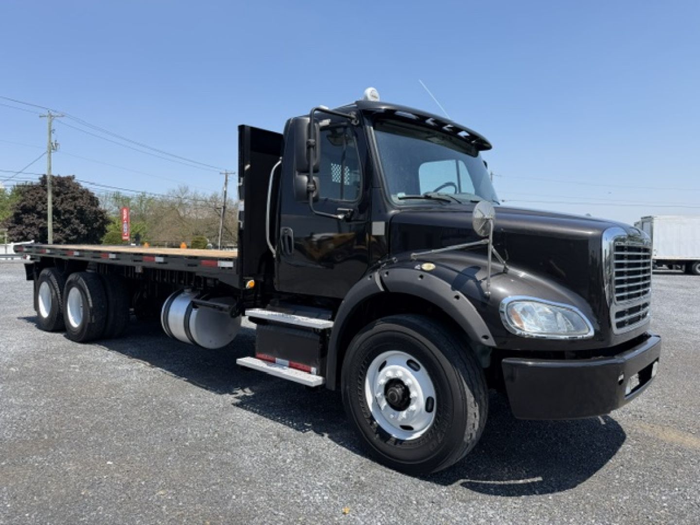 Freightliner M2-112 flatbed truck in black side view showing cab, dual rear wheels, and long flatbed with storage box