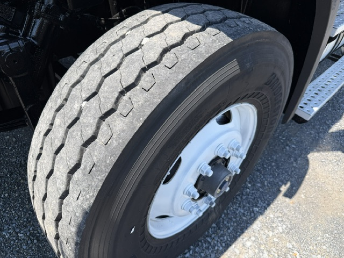 Truck front wheel and fender area of a Freightliner M2-112 showing a large dual rear wheel and white steel rim, tread pattern visible.