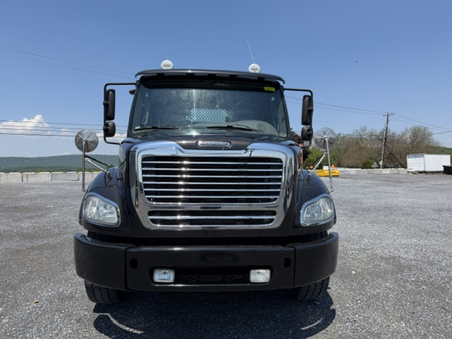 Freightliner M2-112 flatbed truck front view showing chrome grille, bumper, and headlights.