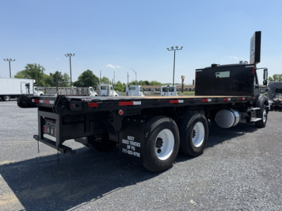 Flatbed truck chassis and rear wheels of a 2016 Freightliner M2-112 flatbed truck, side view showing dual rear axles and fuel tank.