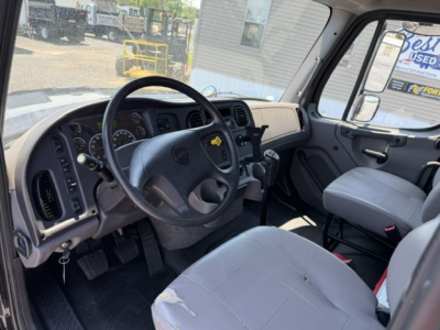 Truck cab interior of a 2016 Freightliner M2-112 showing steering wheel, dashboard, and gray fabric seats.
