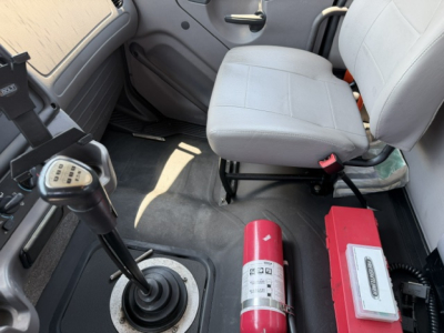Freightliner M2-112 interior cab with manual gear shifter and two seats; red fire extinguisher and another red device mounted near floor; light gray upholstery and door panels visible.