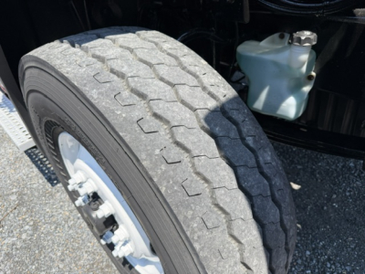 Truck wheel and front tire with visible coolant reservoir and engine bay area; hexagonal tread pattern on tire sidewall.