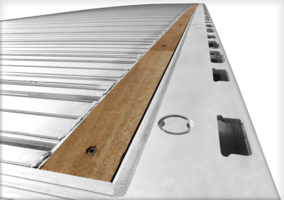 Flatbed trailer edge with aluminum deck and wooden overlay showing tie-down points and stake pockets.