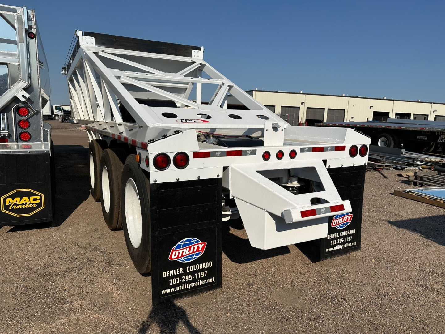 Dump trailer with white frame and black tandem axles. Tail section shows circular lights, US flag sticker, and Utility Colorado contact sticker. Side shows metal framework and ramp.
