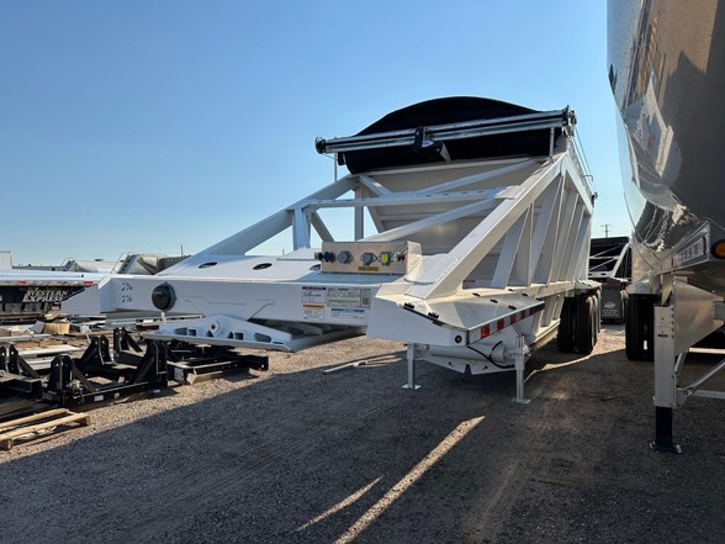 Dump trailer in-service Versa Va with white gooseneck frame and black tarp, side view showing tongue and landing gear.