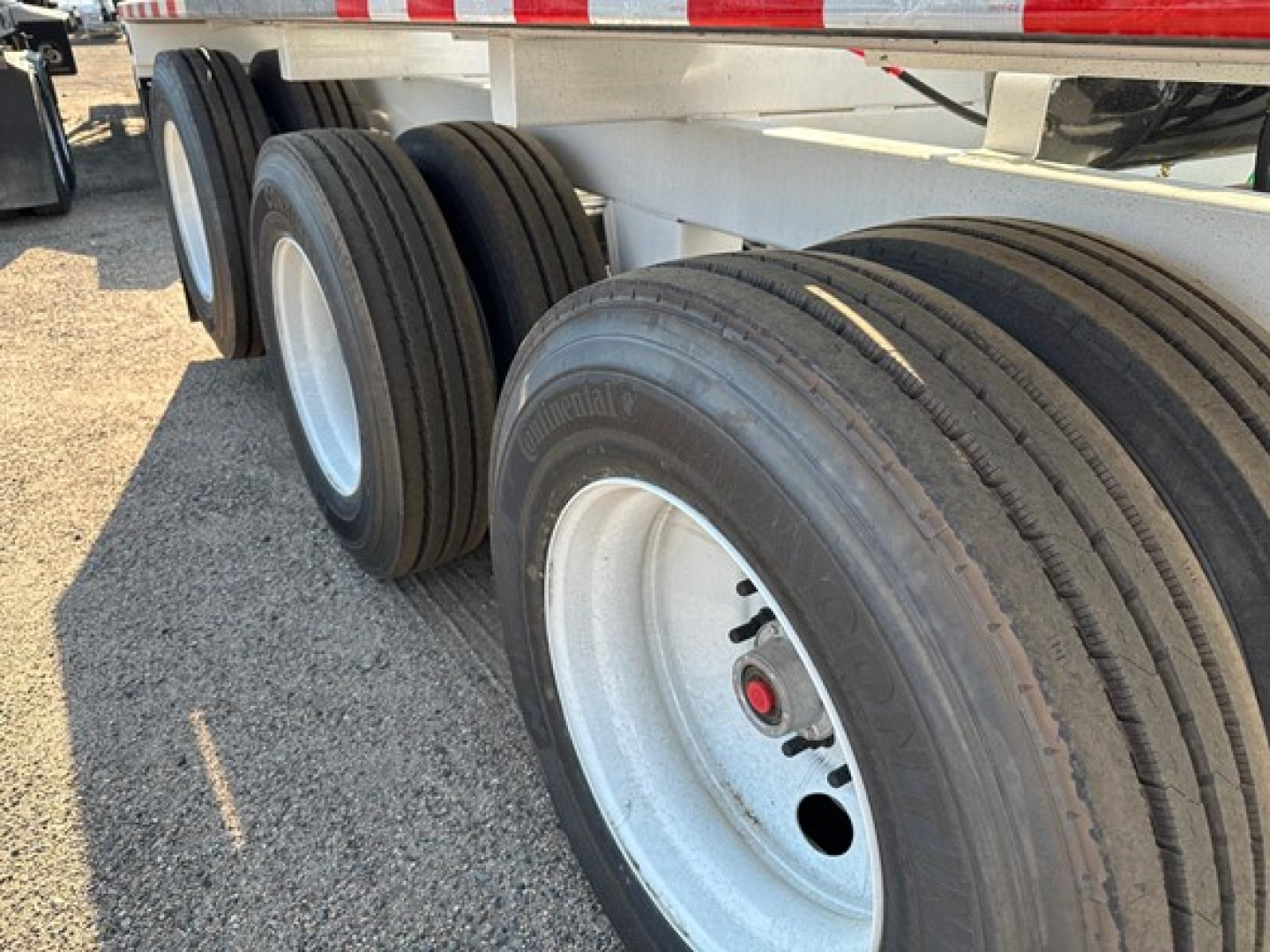 Triple-axle trailer axle set with dual tires and white rims; visible tires and chassis framing under the trailer.