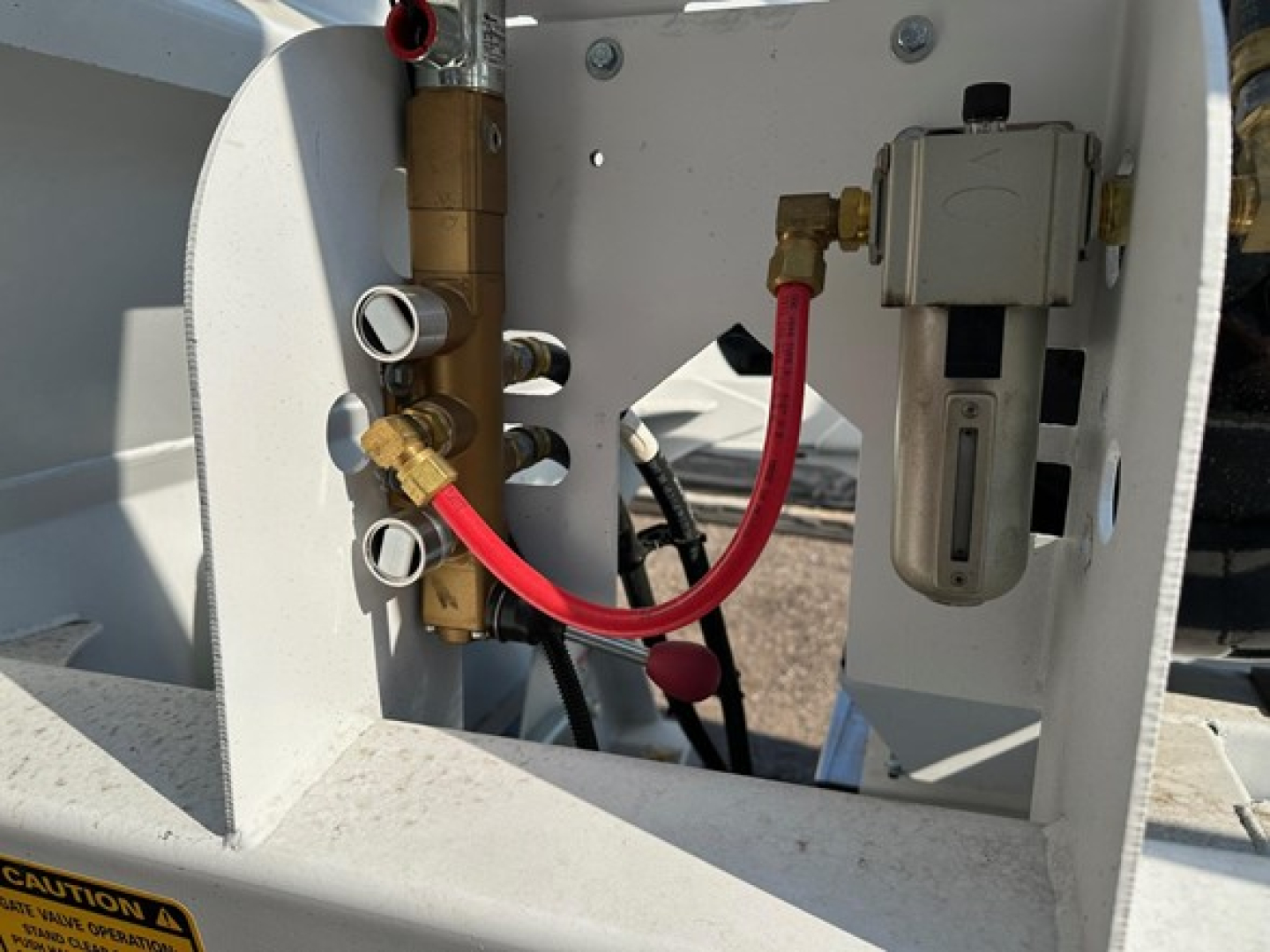 Versa Versa Va trailer compressor/pump area showing brass fittings, red hydraulic lines, and electrical box with gray enclosure.