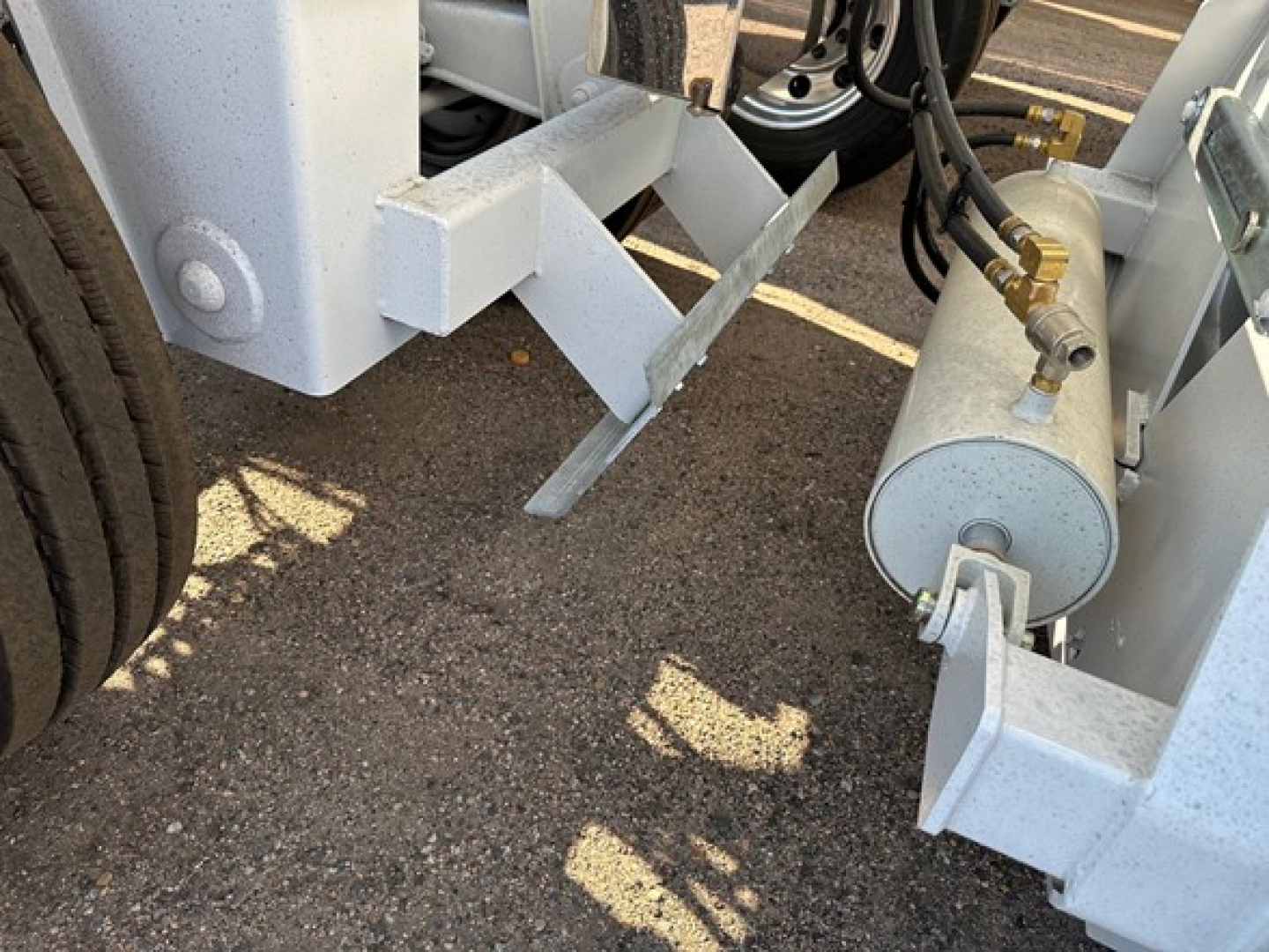 Trailer chassis with hydraulic cylinder and steel frame components visible; close-up of undercarriage area and mounting brackets.
