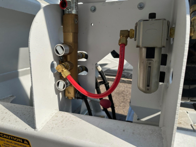 Plateau dump trailer hydraulic control panel with red gauge hose and fittings, electrical valve block, and hydraulic reservoir components visible.