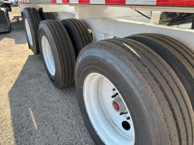 Trailer wheelset showing dual rear axles with three tires on each side and white rims; close-up of tires and hub area under a dump trailer.