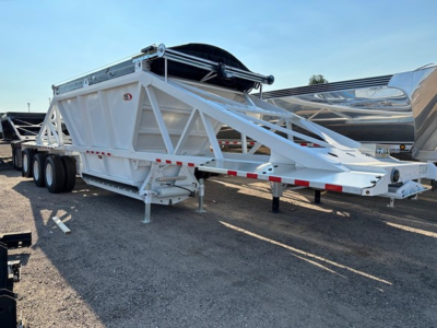 Trailer View showing white Versa Va dump trailer with triangular truss frame and dual axles, long deck, spare tire mounted on top, and reflective safety rails.