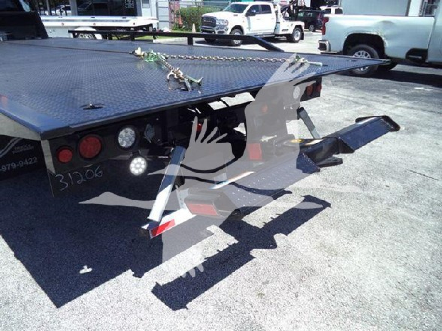 Flatbed tow truck rollback platform with hydraulic ramps and tie-down chains visible, rear view showing metal deck and functional components.