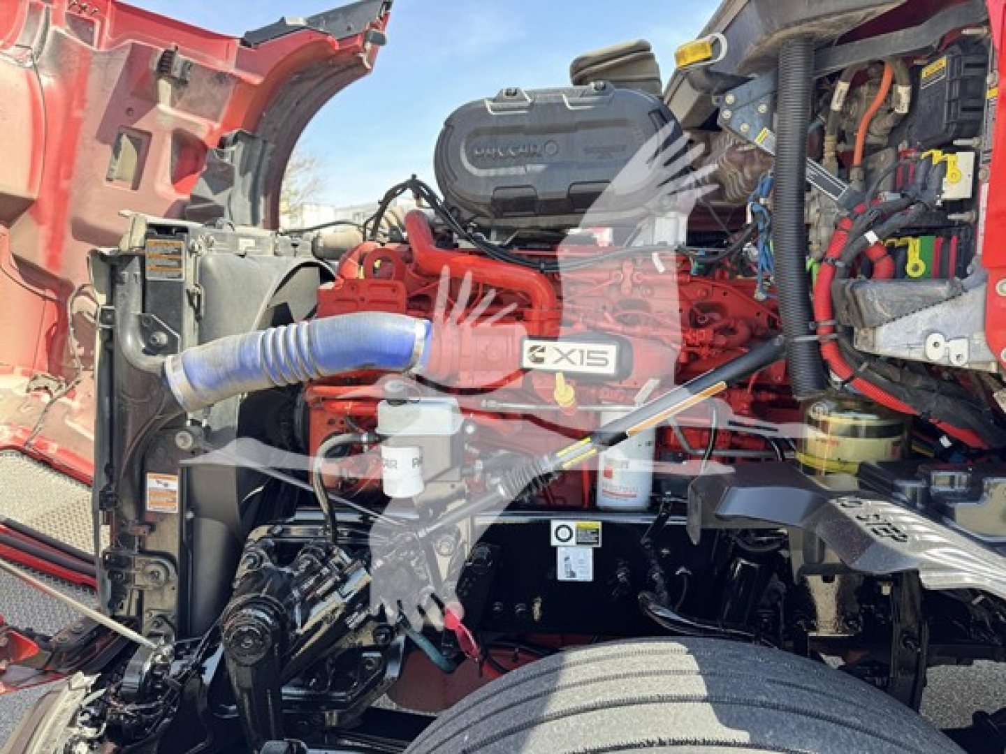 Kenworth T680 engine bay showing Cummins X15 badge and multiple hoses, wiring, and fluid reservoirs.