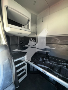 Kenworth T680 interior sleeper cab area showing bunk/storage cabinet and ladder rungs with a chrome grab bar and paneling.
