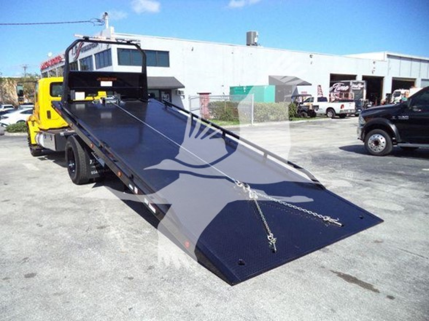 Tow truck with a lowered flatbed in the foreground, International Durastar 4300 rollback truck, VIN 1HTMMMML1KH515548 visible on listing, outdoor lot.