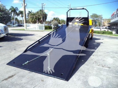 Truck rollback bed with raised ramp in-service: flatblack steel ramp with hinge, trailer hitch area, and yellow cab visible in background.