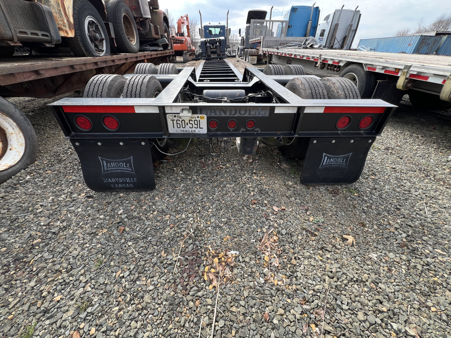 Trailer rear view showing dual axles and mudflaps, license plate T60-59L, red taillights, and a flatbed lowboy trailer frame.