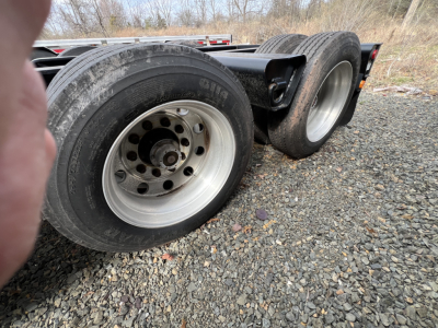 Wheelset of a Landoll lowboy trailer showing dual rear axles with aluminum rims and black tires on a gravel surface.