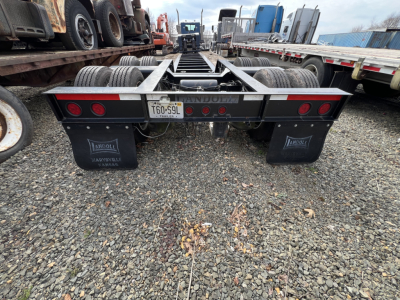 Trailer rear view showing dual axles and mudflaps, license plate T60-59L, red taillights, and a flatbed lowboy trailer frame.