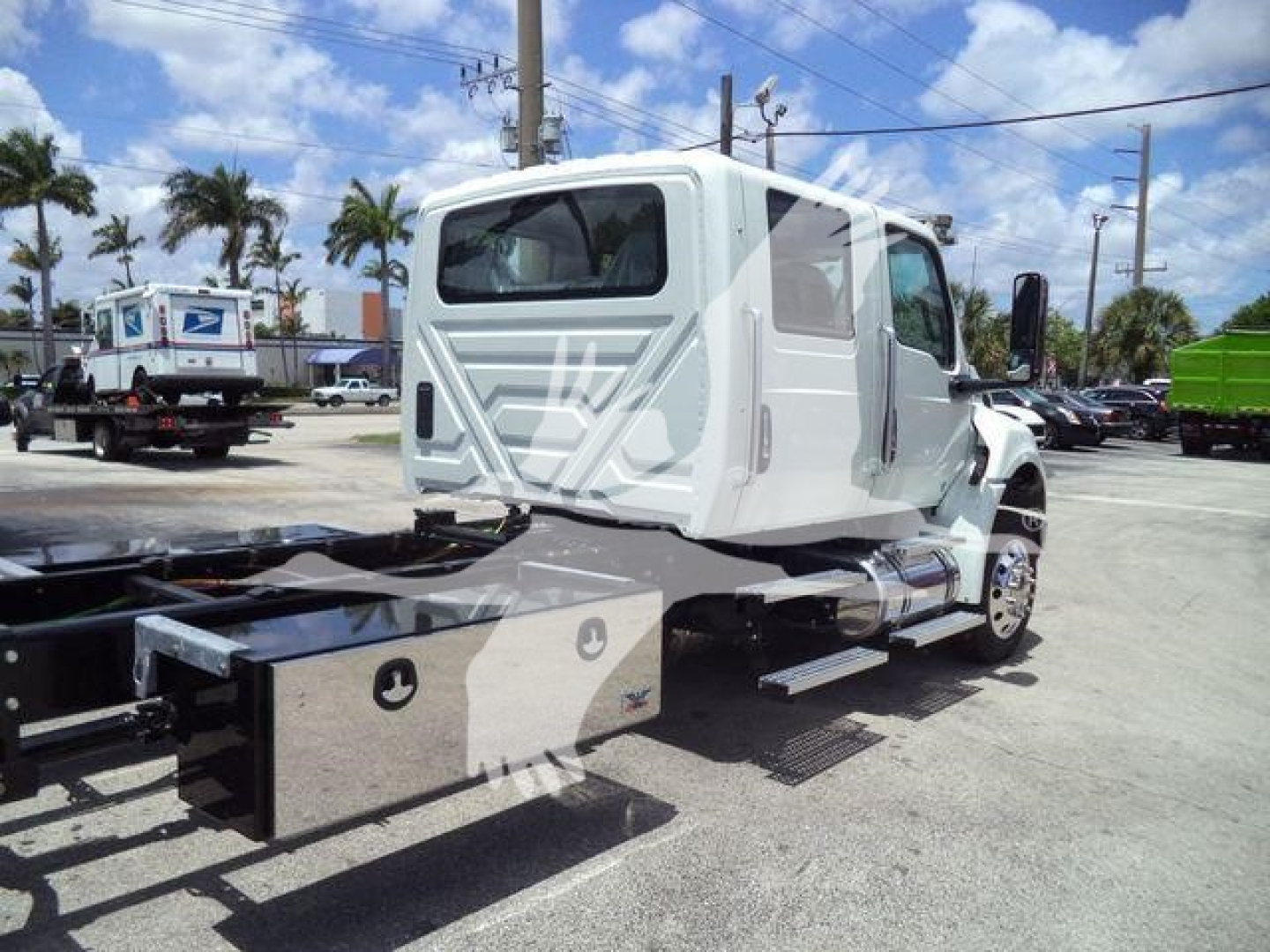 Truck cab of a 2026 International MV rollback truck viewed from rear-left, with steel toolbox and chassis visible.