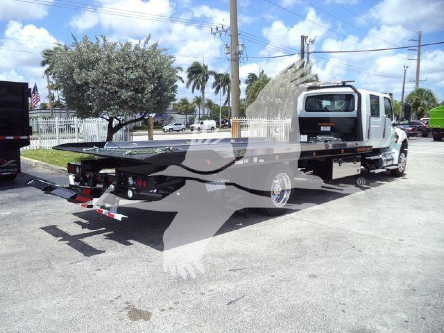Truck with rollback tow bed in a parking lot, International MV model in foreground
