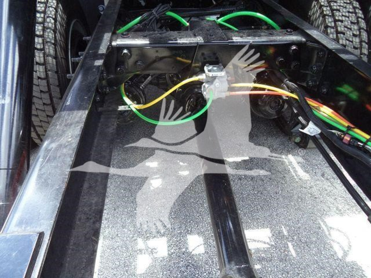 Tractor-trailer chassis with wiring harness and green/yellow cables visible near the frame rails and a metal plate; electrical connectors and a silver fastener; part of a truck undercarriage.