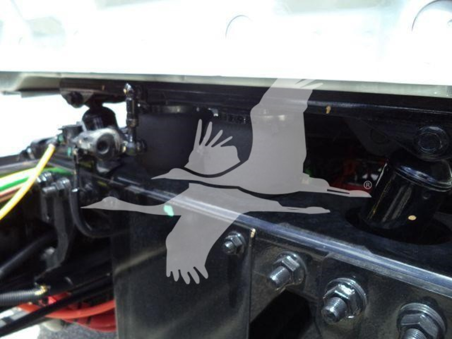 Truck engine bay showing structural frame with bolts and wiring; silhouette image of two birds overlaying the black metal surface.