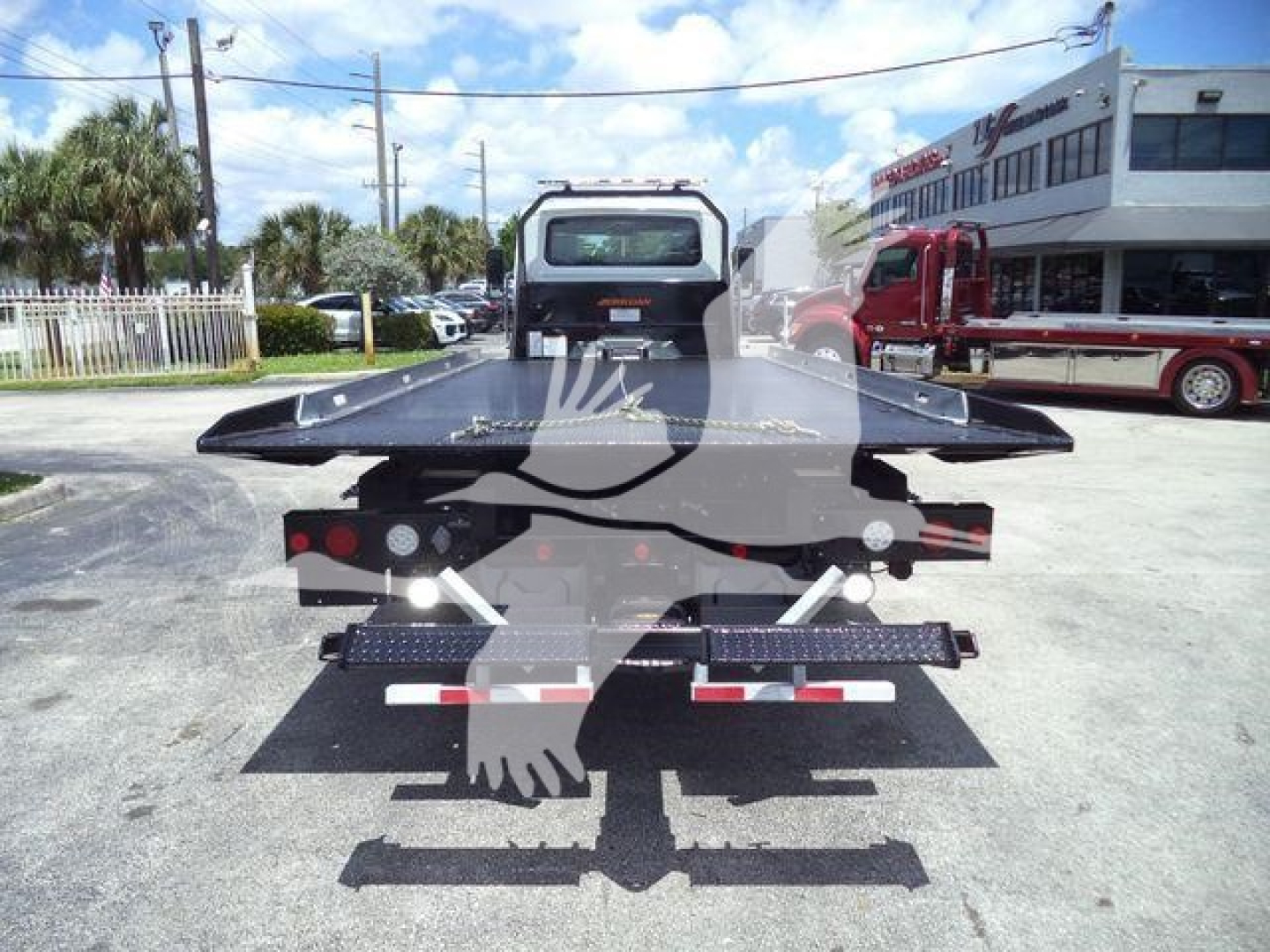 Flatbed tow truck bed with ramps and rear lights as seen from the back in a dealership lot.