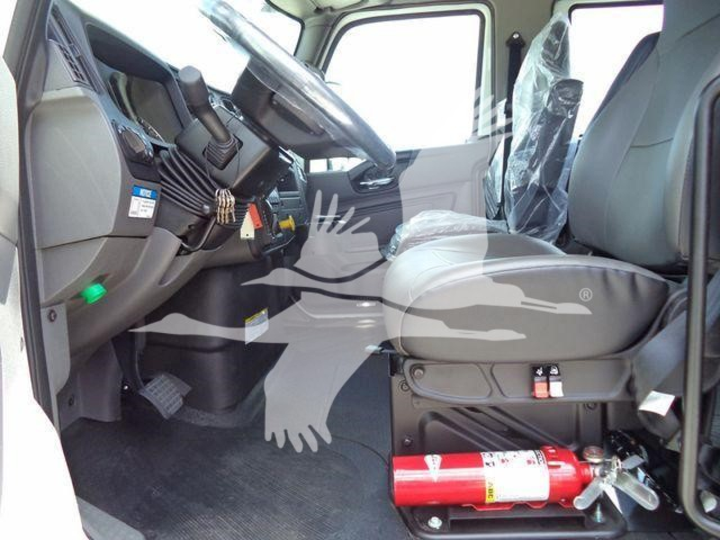 Interior of a truck cab showing steering wheel, driver seat, and dashboard with a red fire extinguisher mounted under the seat area.
