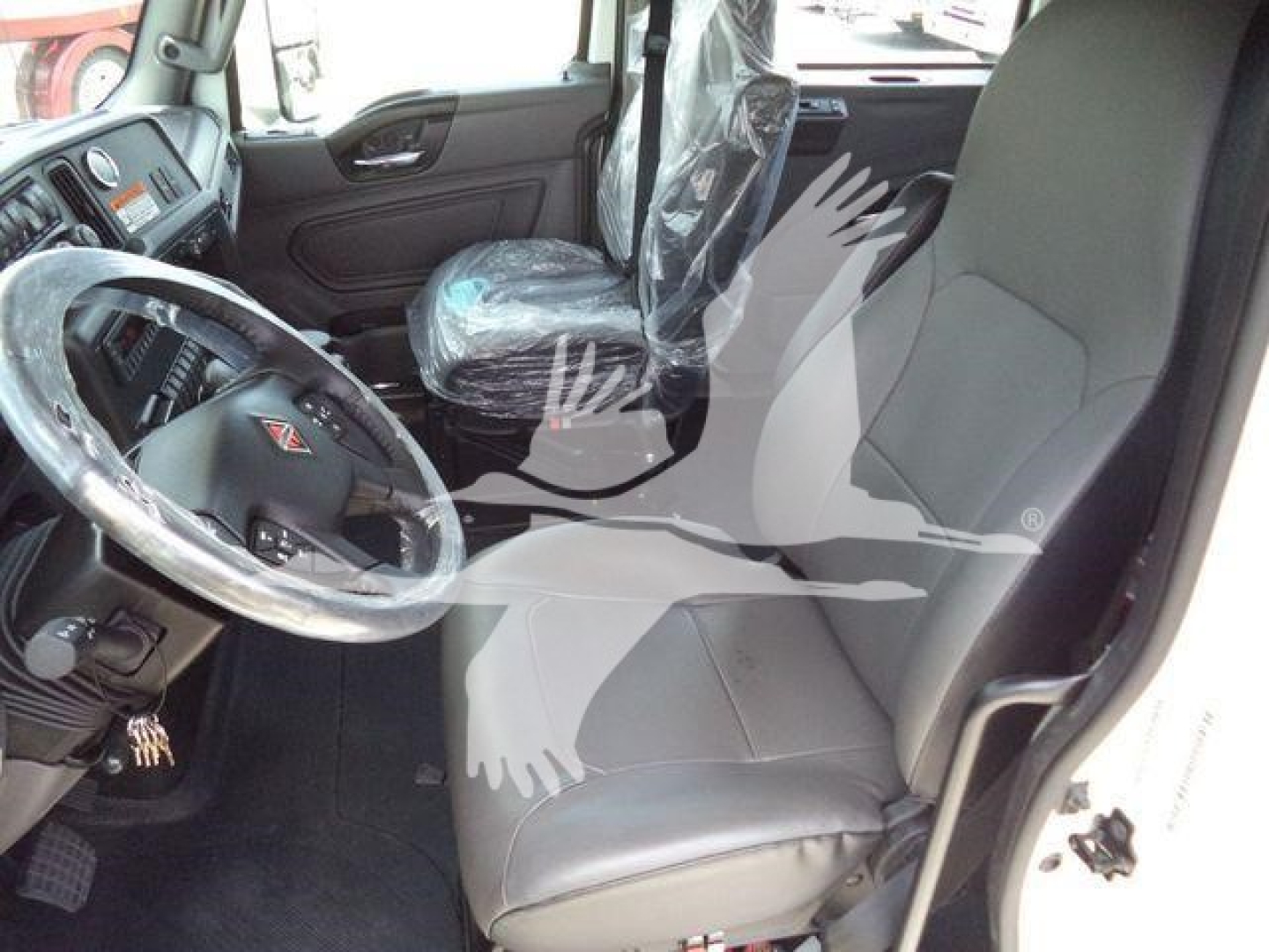 Truck interior showing driver seat and front passenger seat of a new 2026 International MV, steering wheel with factory cover, plastic seat covers.
