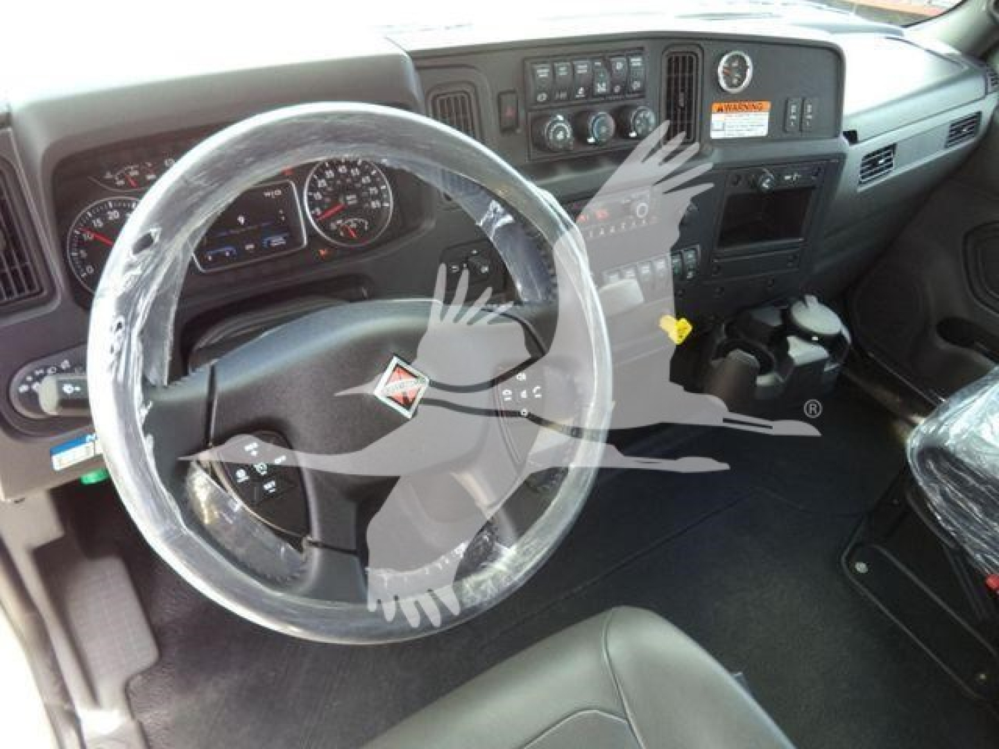 Dashboard and steering wheel view of a 2026 International MV truck interior with wrapped steering wheel and center console controls.