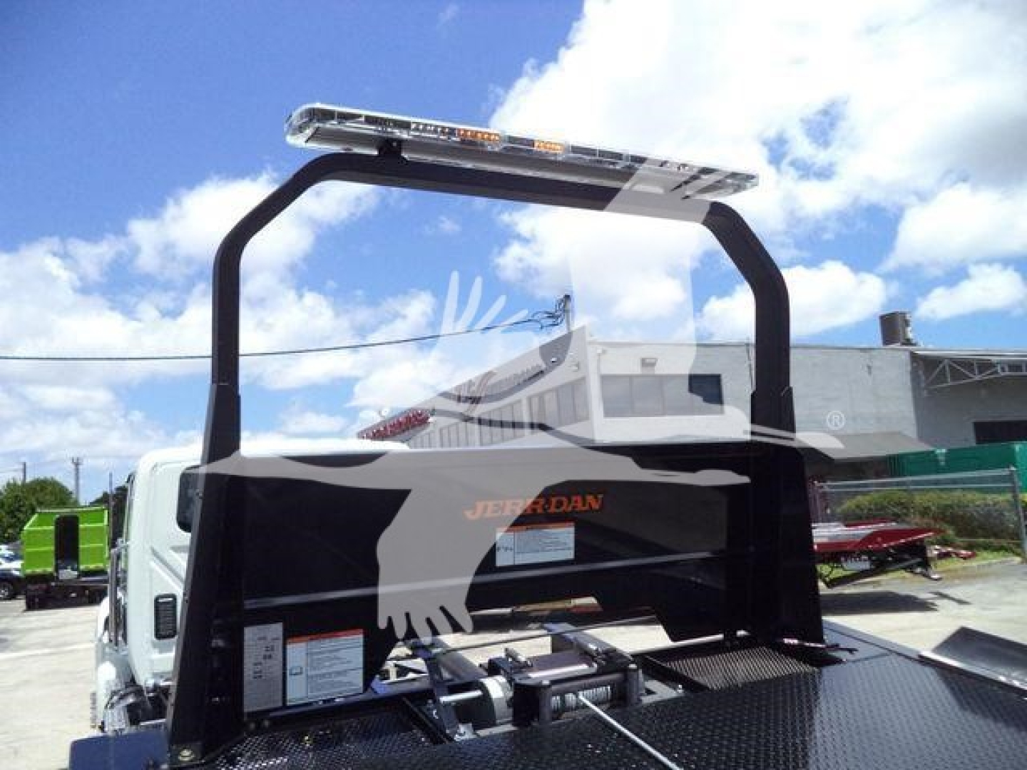 International MV rollback truck with a black rollover protective frame and a light bar mounted above the cab. Flatbed surface visible with coupling and hydraulic components.
