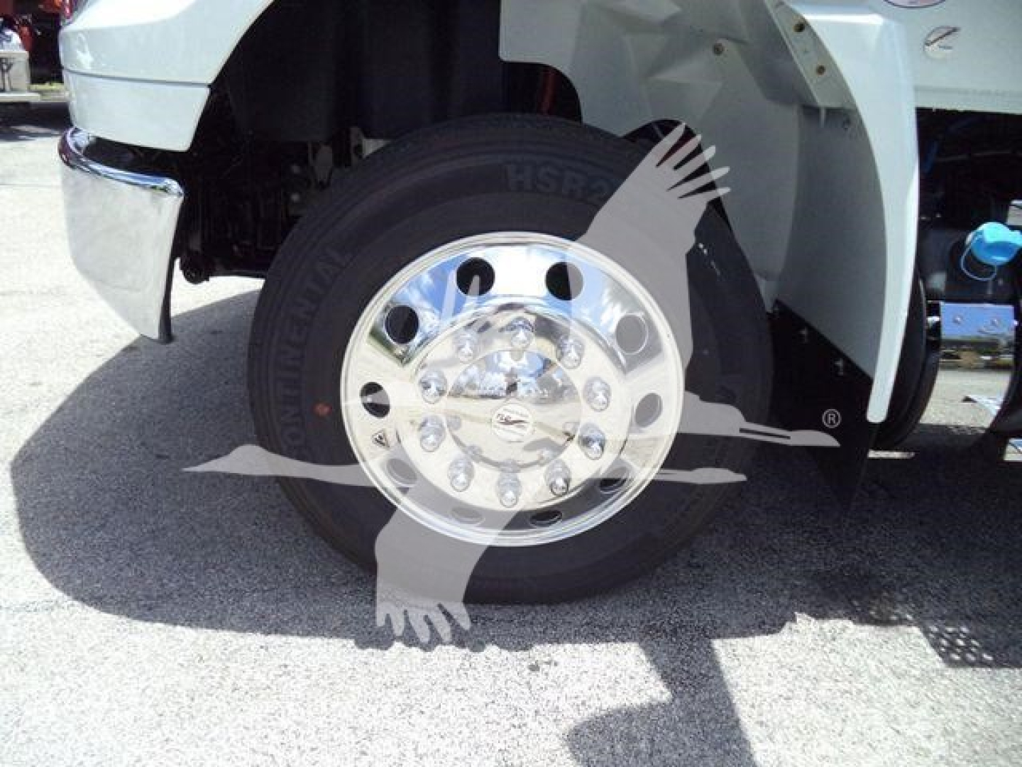 Truck front wheel and fender with chrome wheel, tire, and partial suspension components visible; discusses International MV series rollback truck.