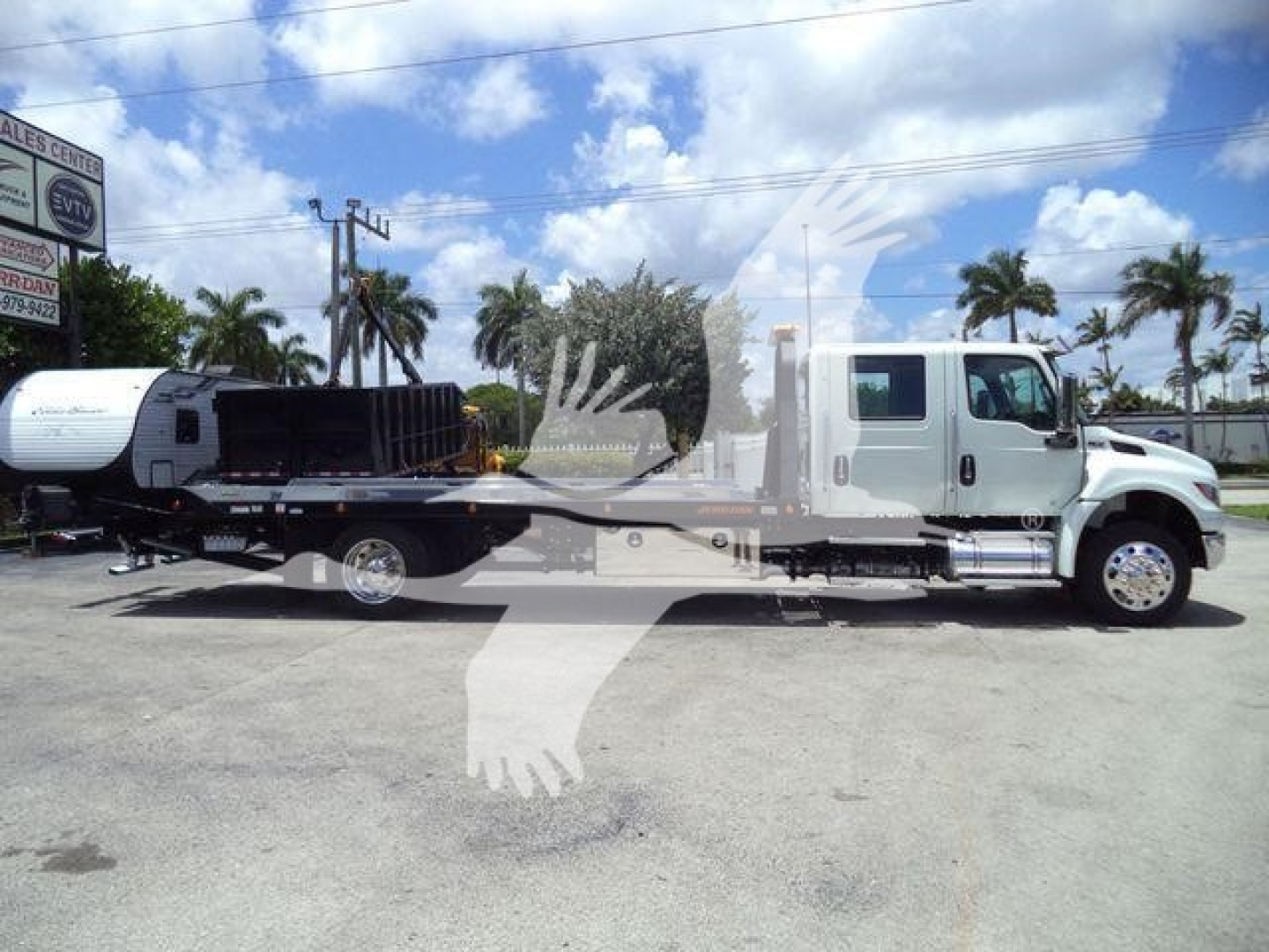 International MV truck in a rollback configuration with a flatbed and hooklift, side view showing cab and chassis, no obvious text legible