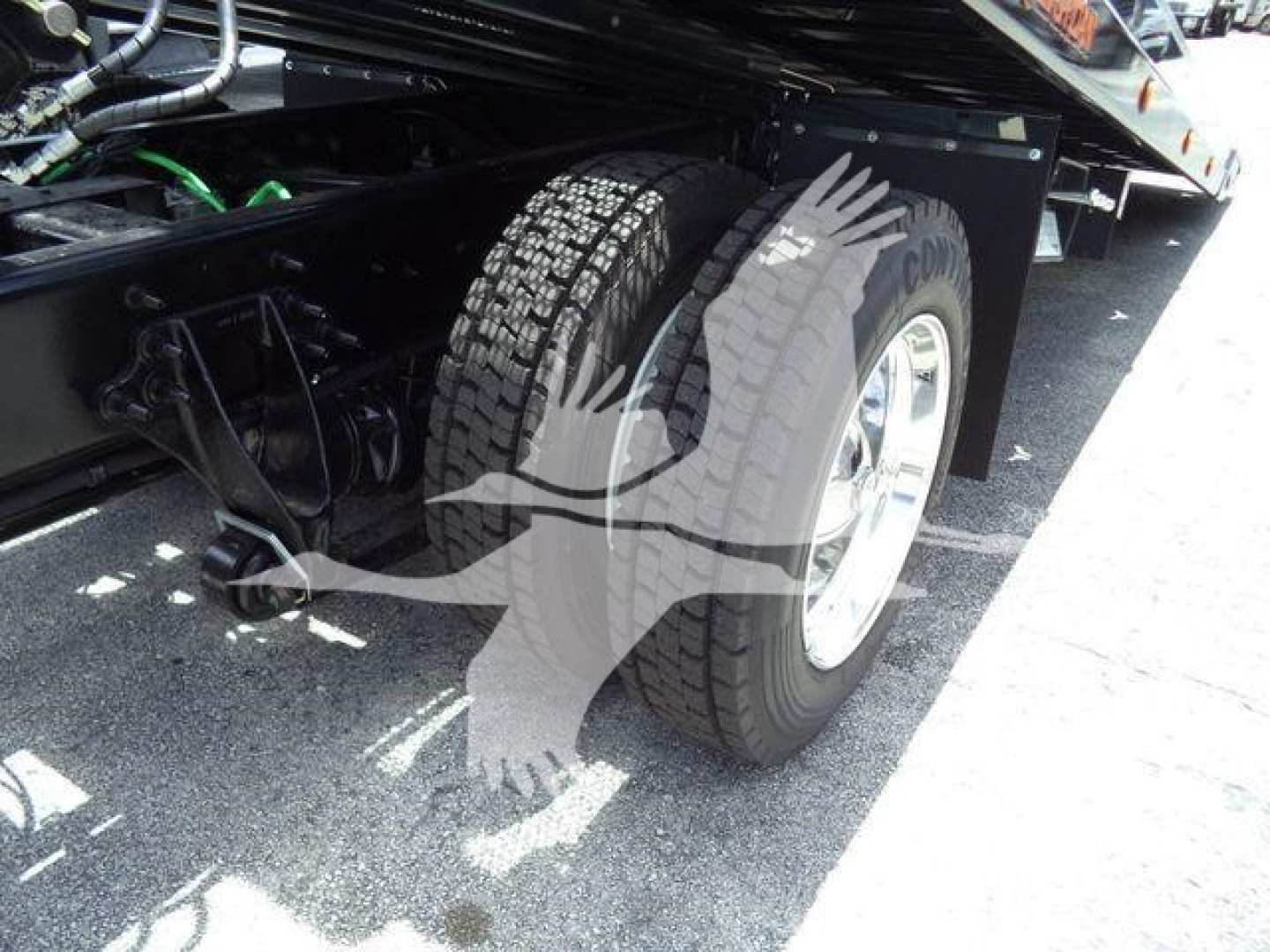 Truck wheel well and rear dual tires of a heavy-duty International MV rollback truck, with a metal frame, hoses, and electrical lines visible beneath the chassis.