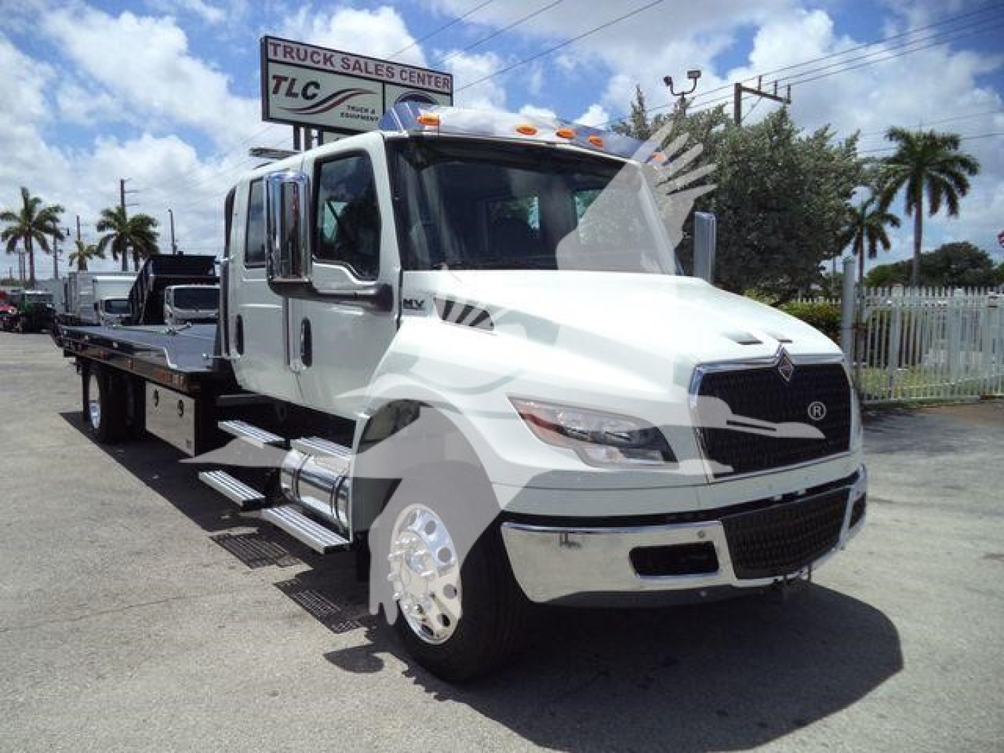 Flatbed tow truck with white cab and black accents, International emblem on grille, side steps, chrome wheels, dealership lot in background.