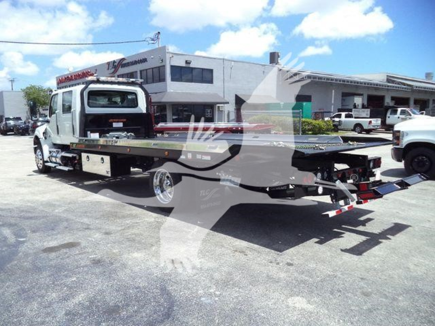 Tow truck flatbed with white cab and long flatbed in a dealership lot, loading equipment, MVCREW stock tag visible