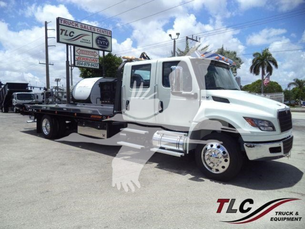 International MV truck in a rollback tow truck configuration showing a white cab and flatbed with chrome wheels and a logo on the lower right.