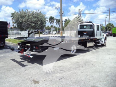 Truck with rollback tow bed in a parking lot, International MV model in foreground