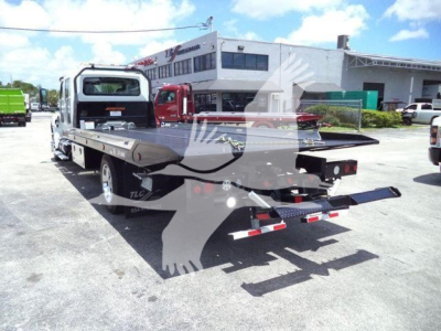Flatbed tow truck rear view showing loading ramps and flatbed in service with side rails and dual rear wheels.