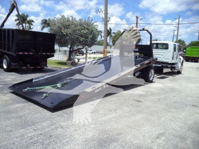 Truck with a low-profile flatbed ramp and a white cab, in-service equipment ready for rollback hauling.