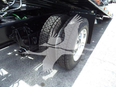Truck wheel well and rear dual tires of a heavy-duty International MV rollback truck, with a metal frame, hoses, and electrical lines visible beneath the chassis.