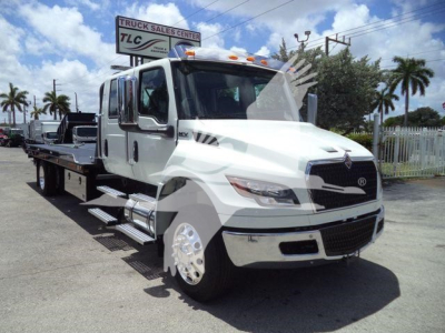 Flatbed tow truck with white cab and black accents, International emblem on grille, side steps, chrome wheels, dealership lot in background.