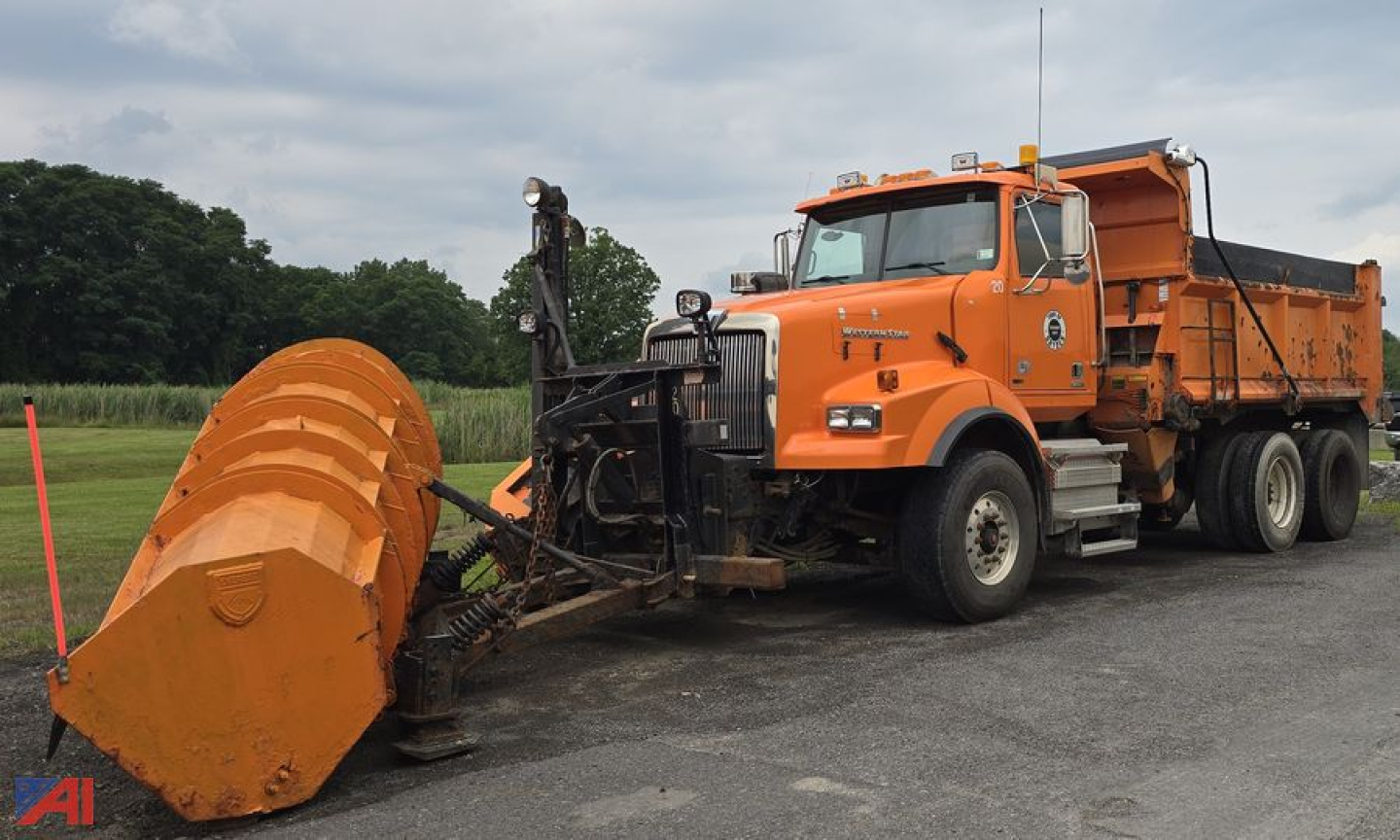 Orange Western Star 4900 SB dump truck with a large orange snow plow attachment in front, dump bed raised slightly, parked on asphalt.