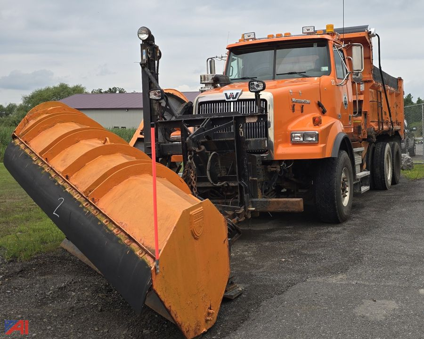 Dump truck with an attached snow plow and large orange scoop parked on asphalt, cab and front grille visible, Western Star emblem on grille.