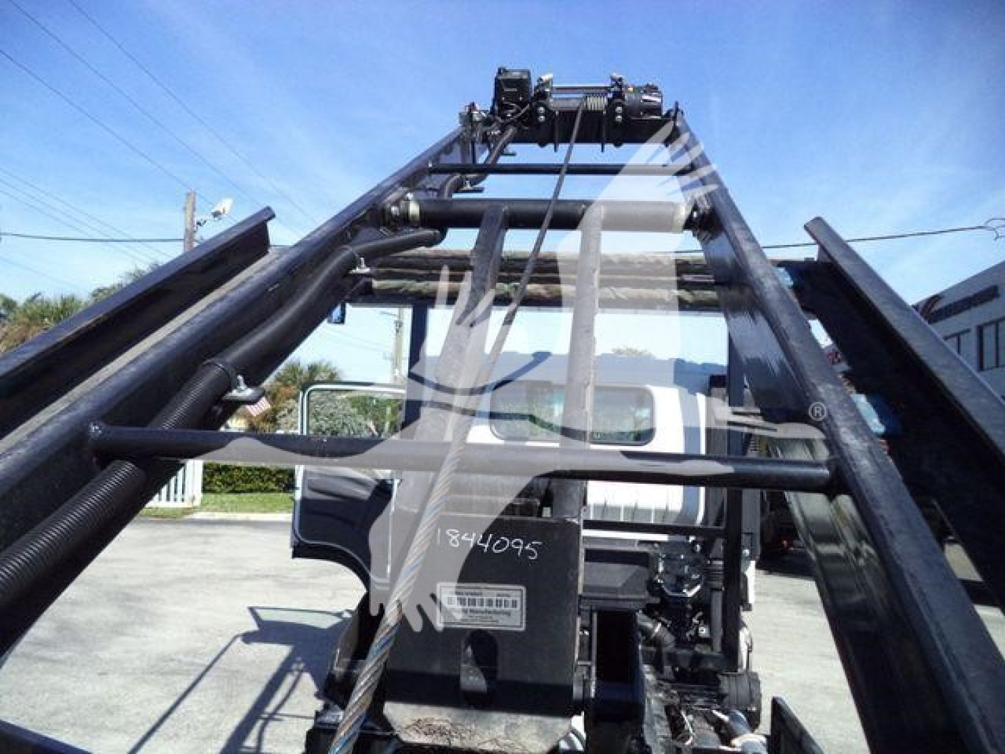 Isuzu NPRR roll-off truck frame with hydraulic arms and cab visible in background.