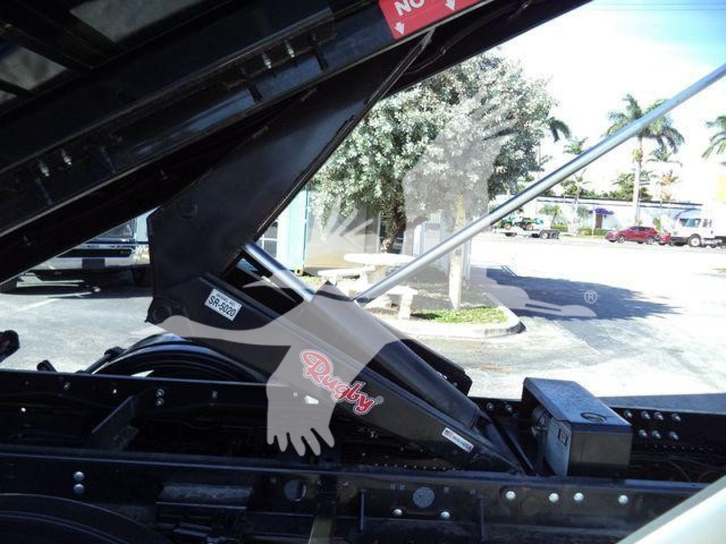 Isuzu NPRR roll-off truck component showing hydraulic strut and wiring with sticker reading 'Ruddy' and glove graphic overlay.